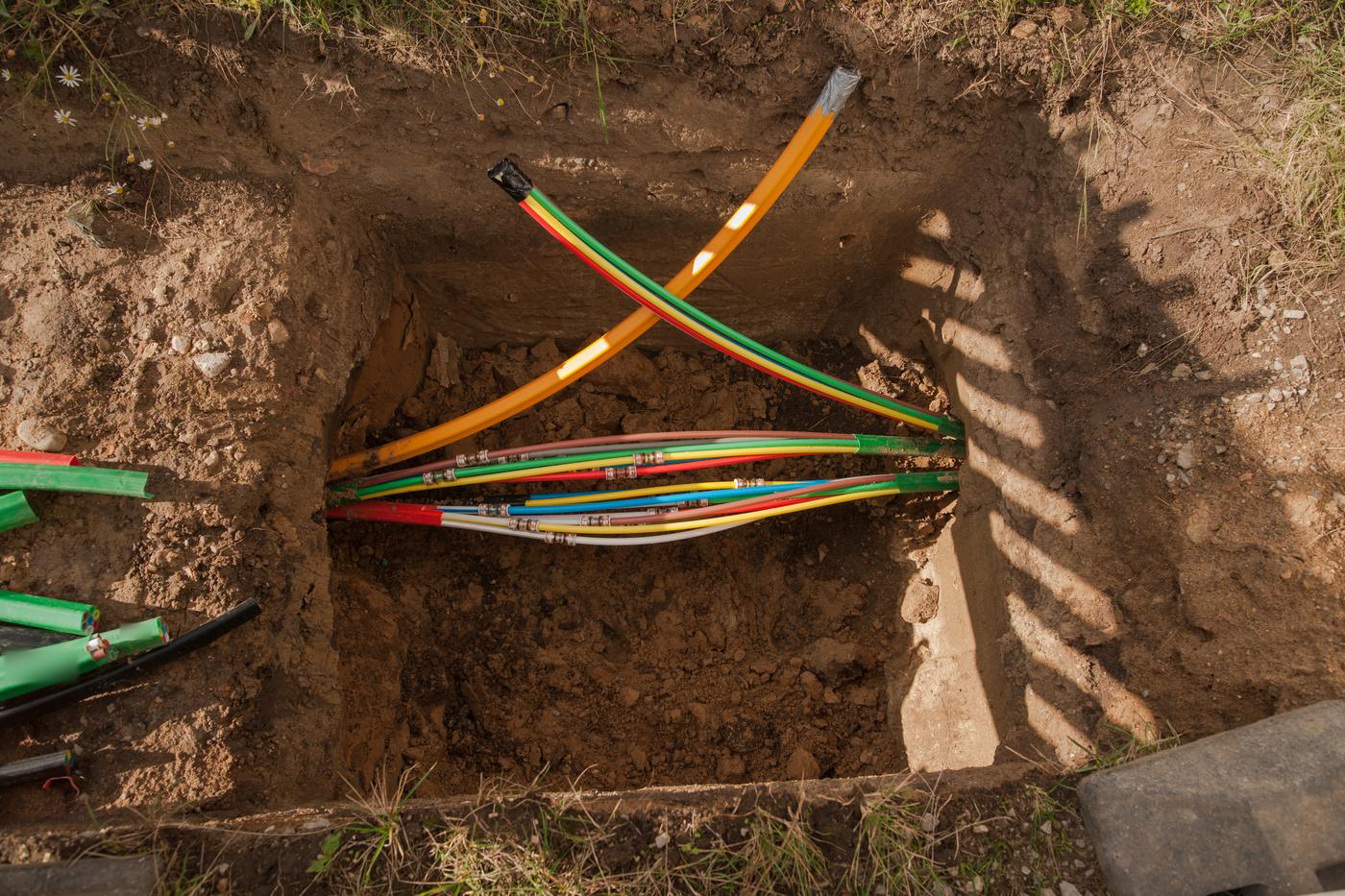 An open bore pit dug into a grassy yard, with colored fiber conduits running through it