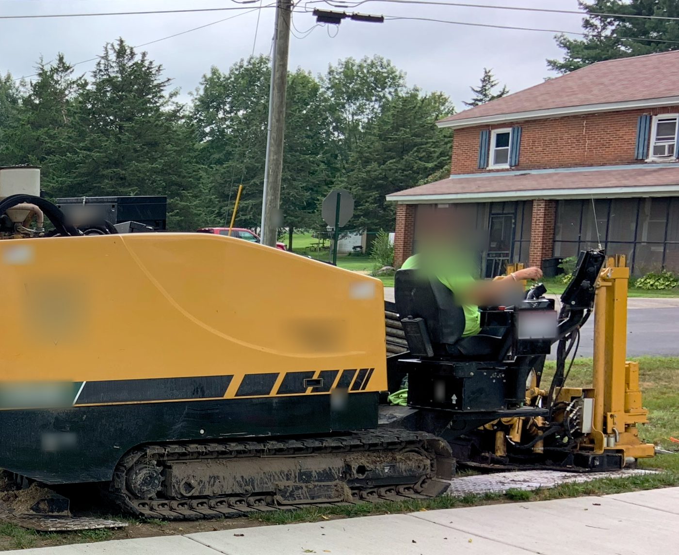 A horizontal directional drilling rig boring along the grass strip of a residential street, with houses in the background